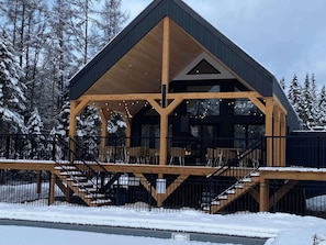 A wooden cabin with a balcony, stairs, and a view of snow-covered trees.