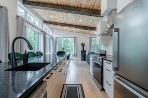 A modern kitchen with a large island, stainless steel appliances, and a wooden ceiling. - Villa Le Frigg | Private Spa • Pet Friendly (Shannon)