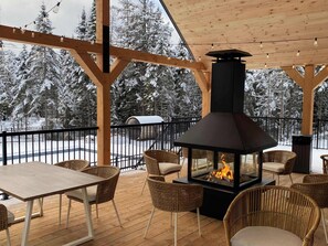 A covered outdoor seating area with a wood-burning stove, wicker chairs, and a view of snow-covered trees. - Villa Le Frigg | Private Spa • Pet Friendly (Shannon)