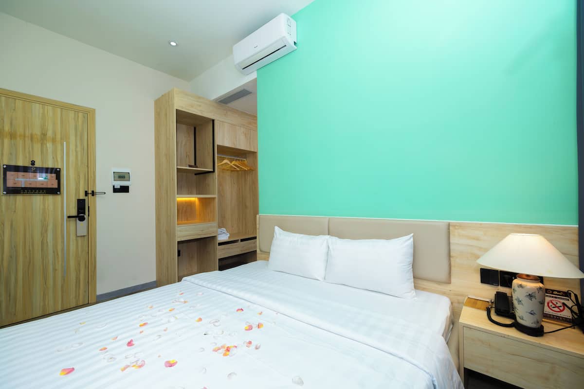 Quarto de hotel com cama, mesa de cabeceira, guarda-roupa de madeira e parede verde.
