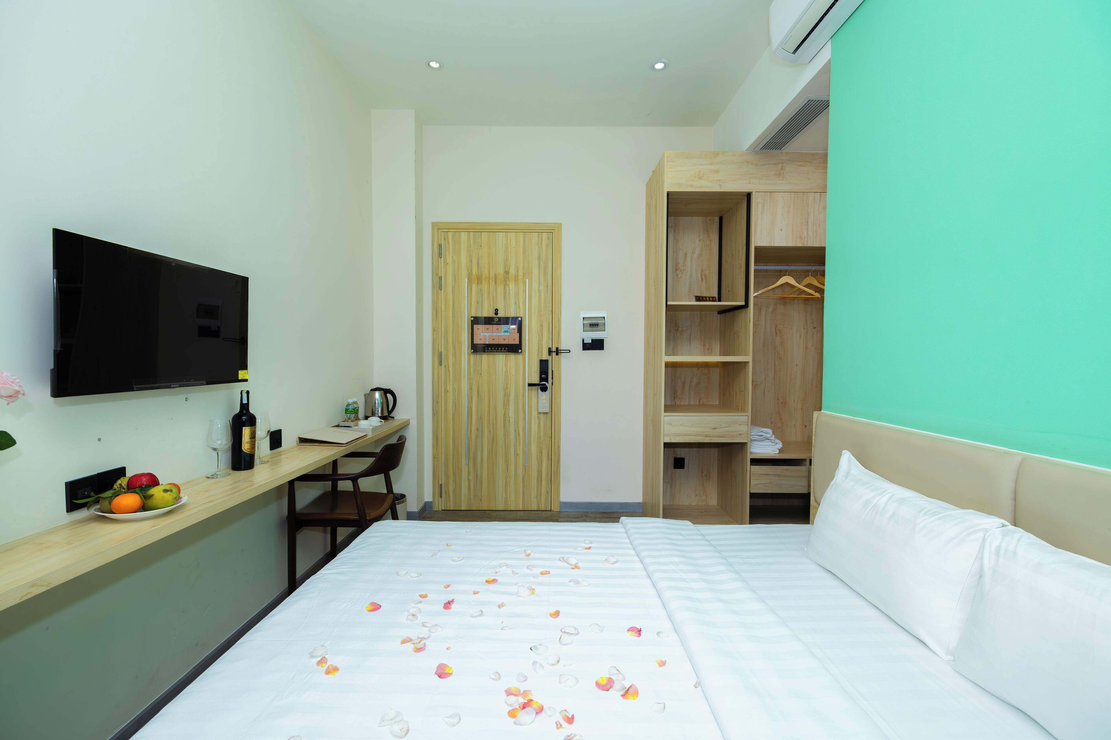 A hotel room with a bed, a TV, a wooden desk with a chair, and a wardrobe.
