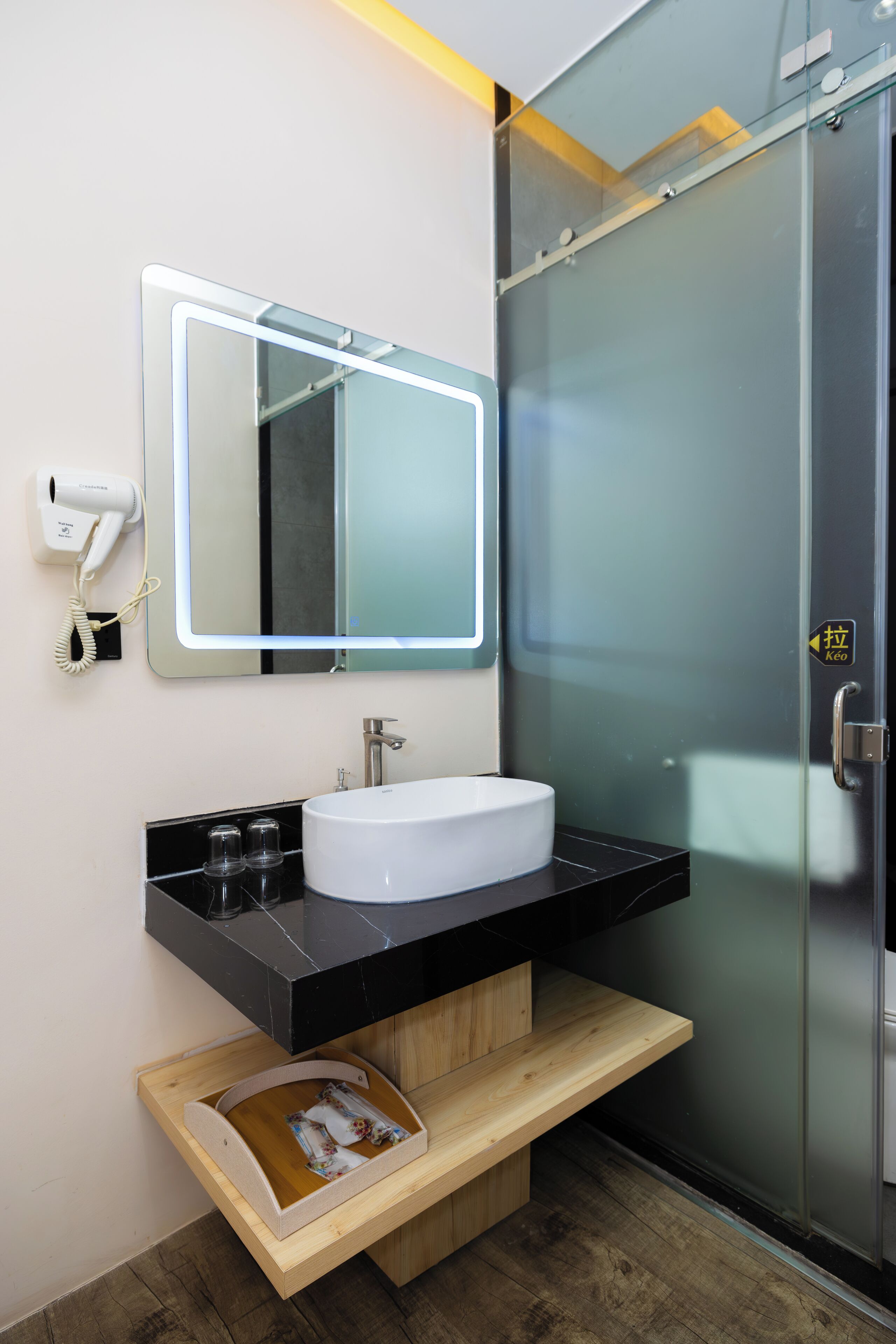 Une salle de bain moderne avec un lavabo blanc, un plan de toilette noir et un miroir doté d’un cadre éclairé.