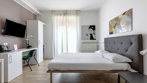 Une chambre d’hôtel moderne équipée d’un lit, d’un bureau, d’une chaise, d’une télévision et ornée d’œuvres d’art sur les murs.