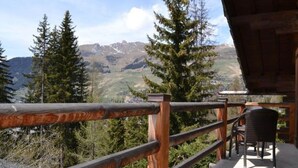 Una terraza de madera con barandilla de metal, con vistas a un paisaje montañoso con pinos.