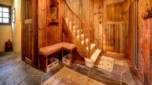 Un interior de madera con suelo de piedra, un banco de madera, una escalera y una puerta.