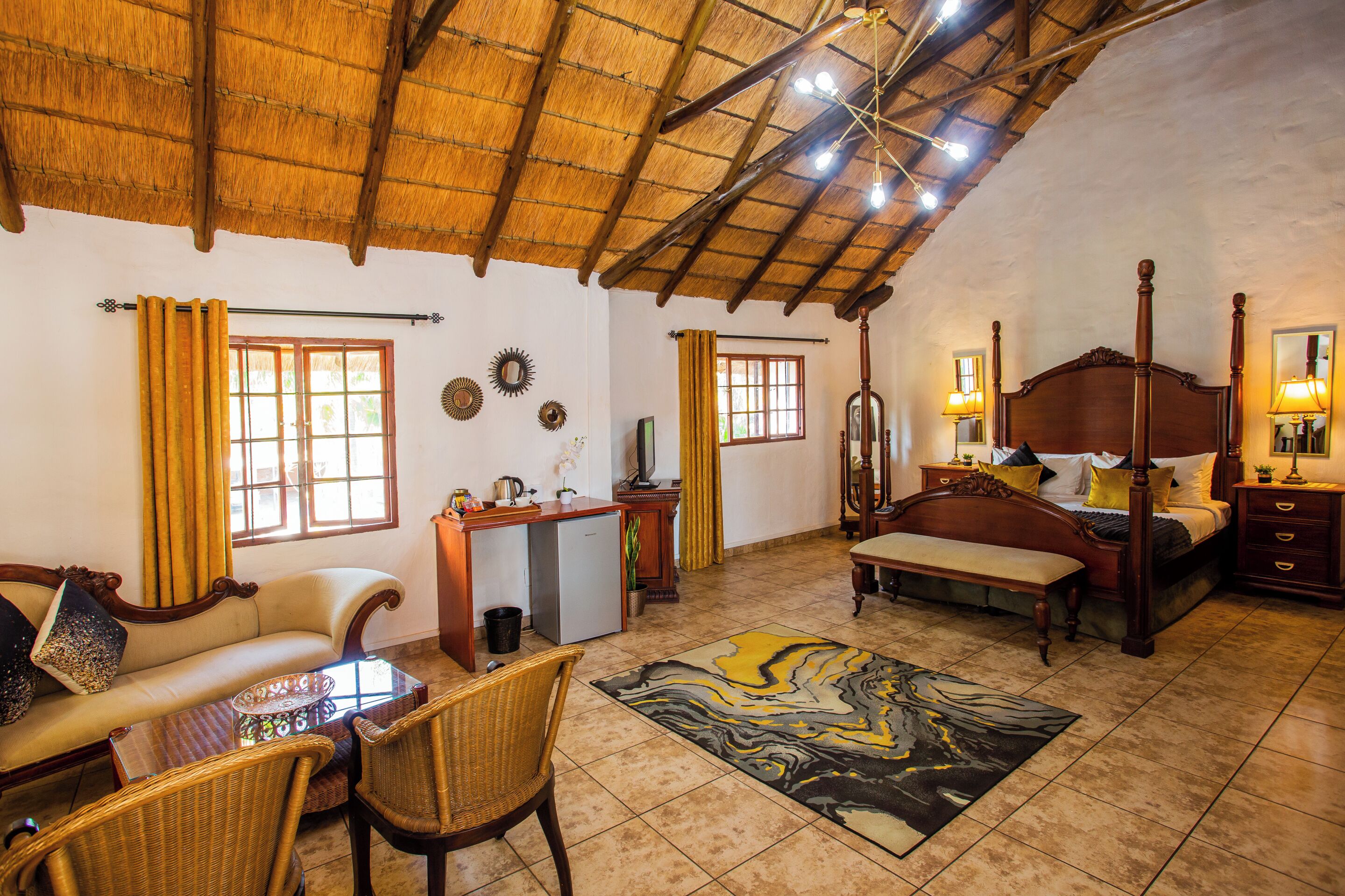 A spacious room with a high ceiling, a bed with a wooden headboard, a sofa, a dining table with chairs, and a small desk.