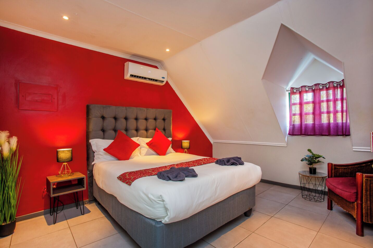 Une chambre moderne avec un grand lit, des murs rouges et un plafond en pente.