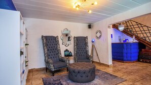 Un vaste espace de vie agrémenté de deux fauteuils décoratifs, d’un pouf capitonné et d’un luminaire moderne.