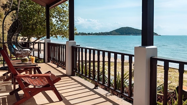 A covered outdoor seating area with a view of the sea and a distant mountain. - Satva (Koh Samui)