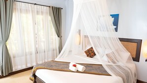 A hotel room with a bed, a canopy, a nightstand, a lamp, and a framed picture on the wall. - Satva (Koh Samui)