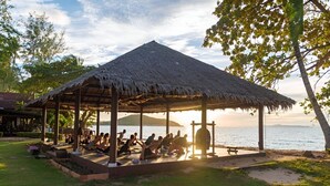 A thatched-roof pavilion with people practicing yoga on mats, overlooking a body of water. - Satva (Koh Samui)