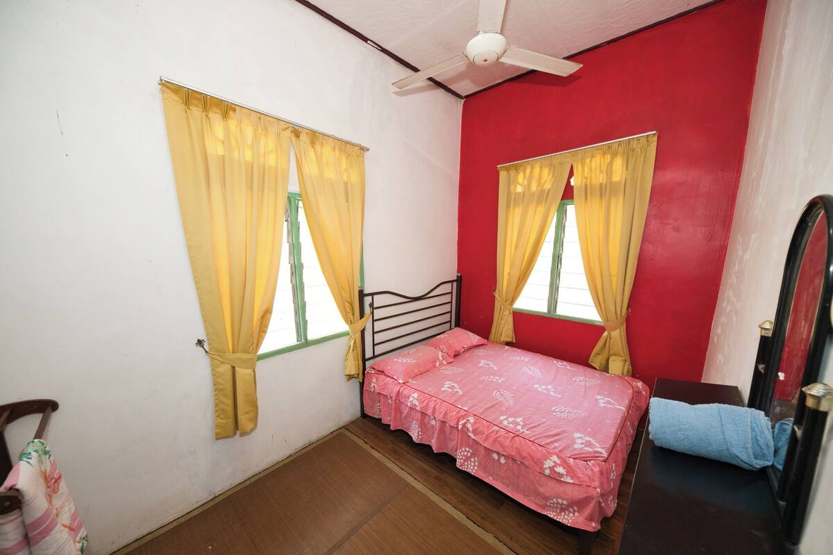 A room with two beds, yellow curtains, a ceiling fan, and a red wall.