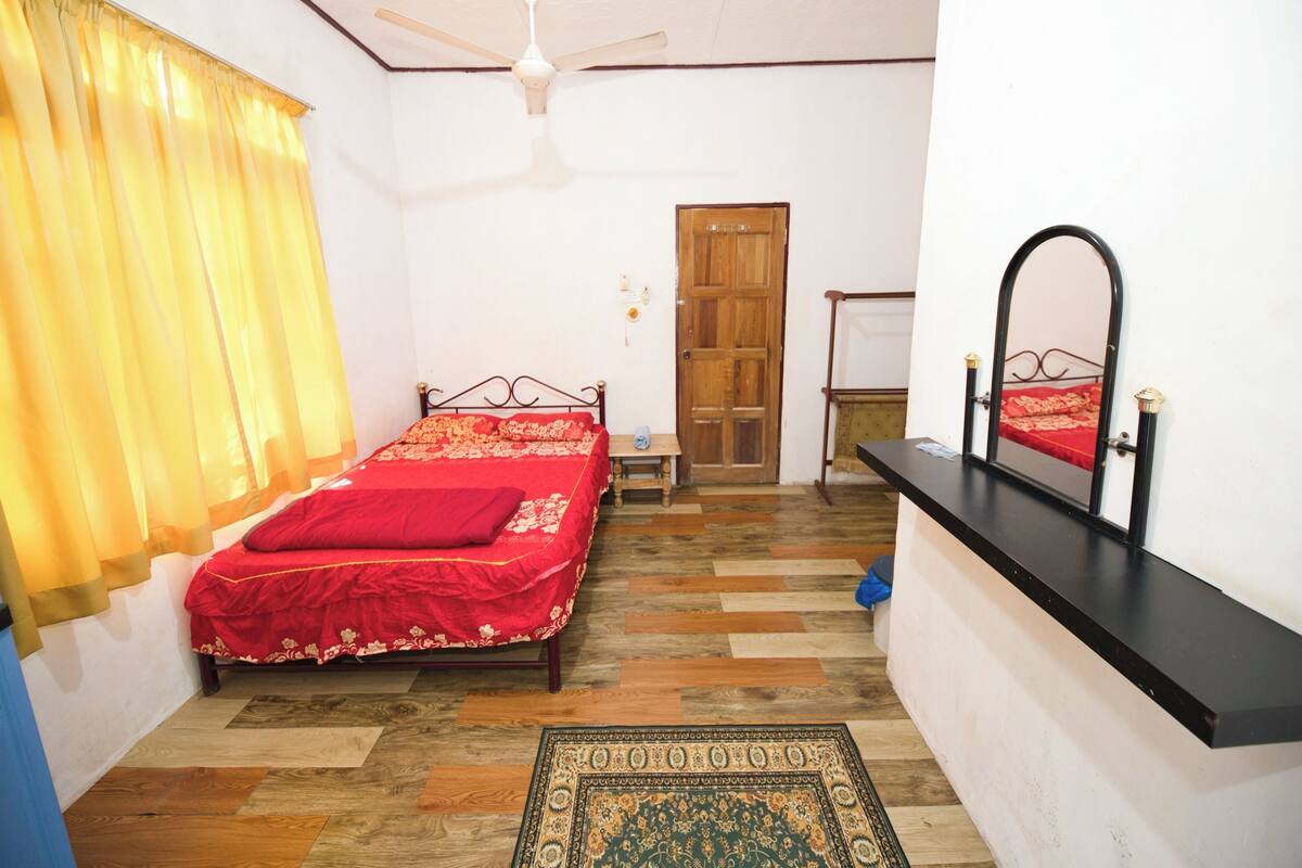 A bedroom with a bed, a ceiling fan, a wooden door, a mirror, and a patterned rug.