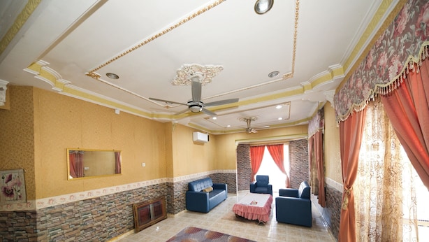 A spacious living room with a stone accent wall, a ceiling fan, and a large window with red curtains. - OYO 90990 Sri Tempurung Homestay (Chukai)