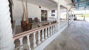A covered outdoor area with a tiled floor, wooden furniture, and a white railing. - OYO 90990 Sri Tempurung Homestay (Chukai)
