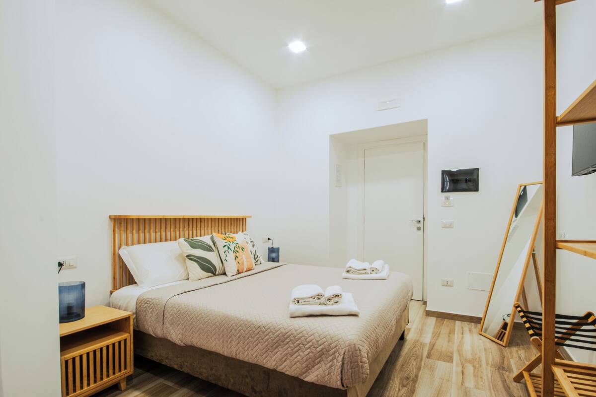 A neatly arranged bedroom with a bed, bedside table, and a wooden shelf unit.