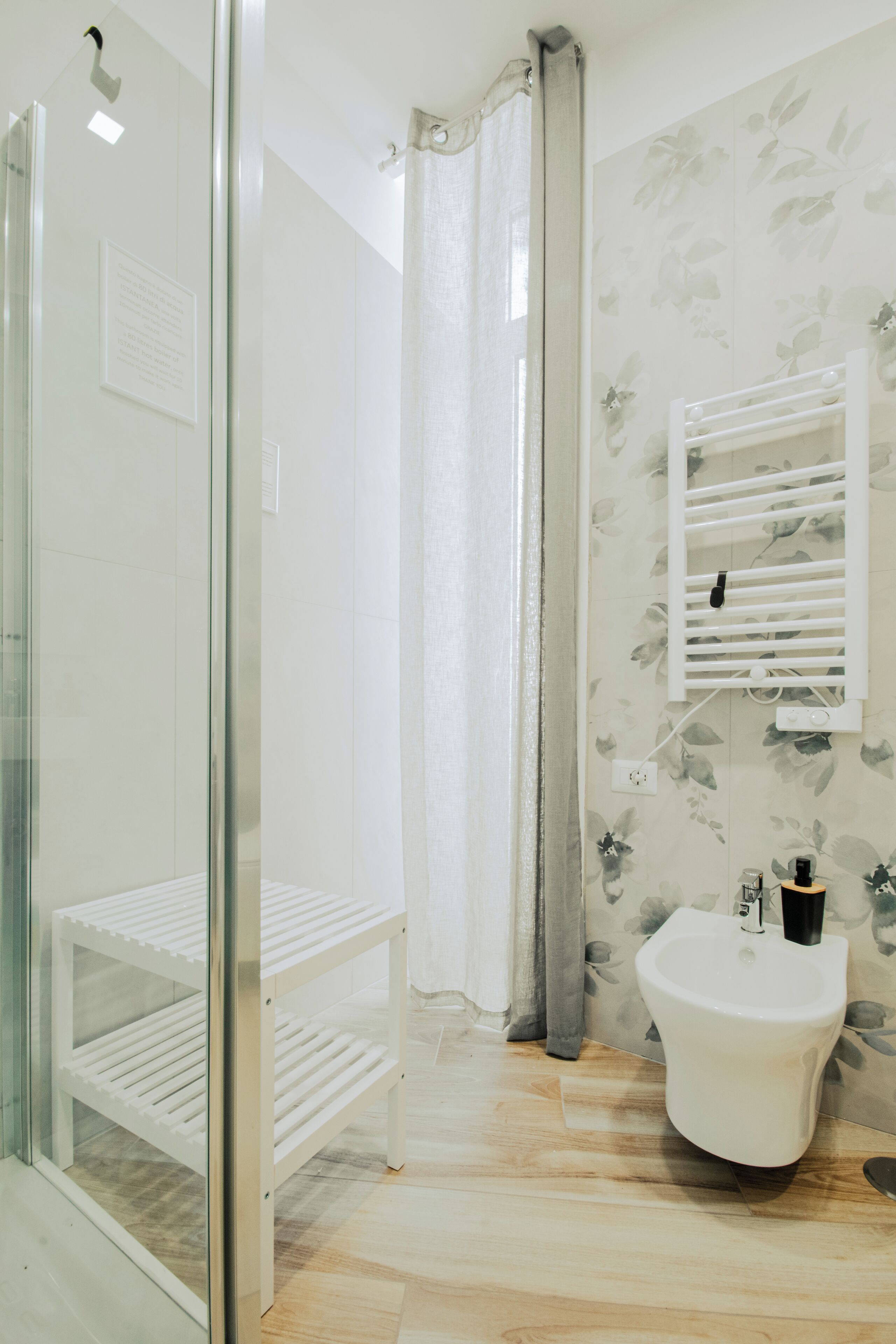 A bathroom with a glass shower enclosure, a white sink, and a shelf with toiletries.