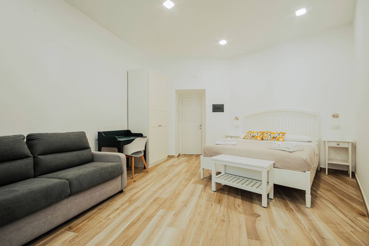 A modern bedroom with a bed, a sofa, a desk, and a small table.
