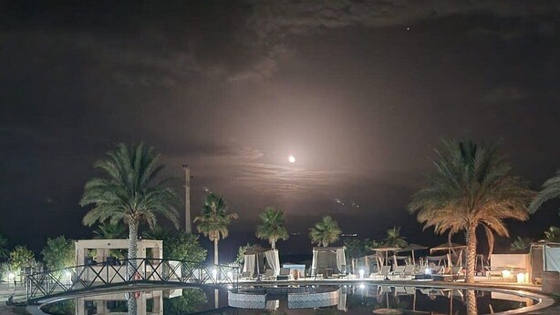 Ein Poolbereich eines Resorts bei Nacht, mit Palmen, einer Brücke und einem von Mondlicht beschienenen Himmel.