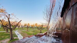Ein Wasserfall stürzt über eine Holzkonstruktion in einem Park mit Wegen und Bäumen.