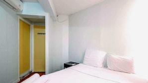 A hotel room with a bed, a nightstand, a rolled towel, and a door leading to another room. - Apartemen Taman Rasuna 2BR. 80sqm (Jakarta)