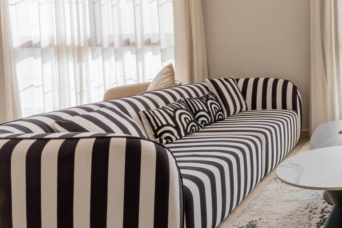 A modern living room with a striped sofa, a round coffee table, and sheer curtains.