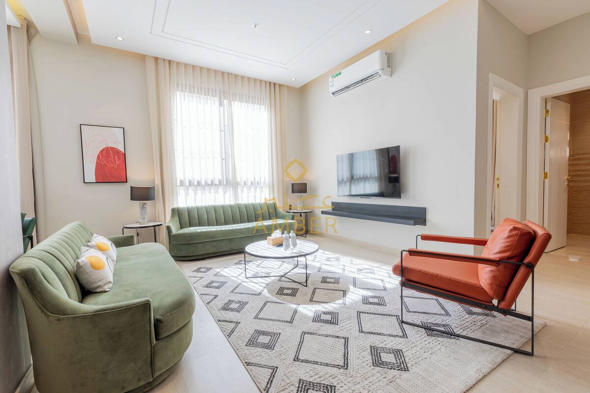 A modern living room with a green sofa, a red armchair, and a patterned rug.
