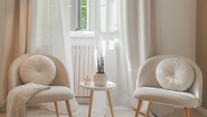 A room with two chairs, a small table with a vase and plant, and a window with sheer curtains. - The Printers Home in Como (Como)
