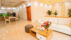 Una sala de estar moderna con un sofá blanco, una mesa de centro de madera con adornos, y un comedor con una mesa y sillas de madera.