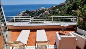 A terrace with two lounge chairs and a small table, overlooking a coastal town and the sea. - Casa FeFe a scenic view of Positano and a swimming pool! (Positano)