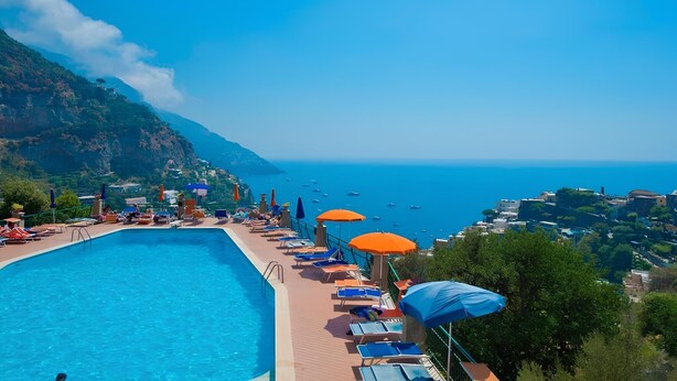 A poolside area with lounge chairs and umbrellas, overlooking a coastal town and the sea. - Casa FeFe a scenic view of Positano and a swimming pool! (Positano)