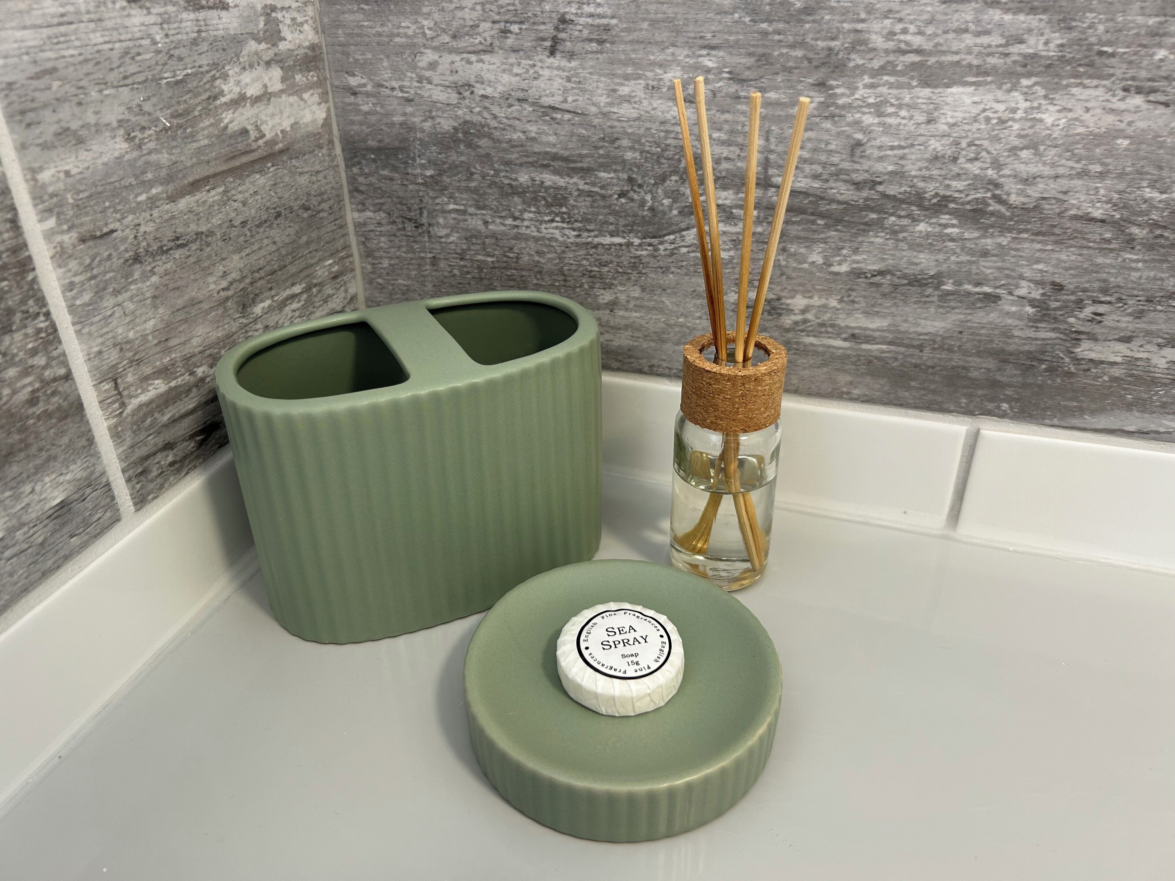 A bathroom with a green soap dispenser, a bottle of sea spray, and reed diffusers.