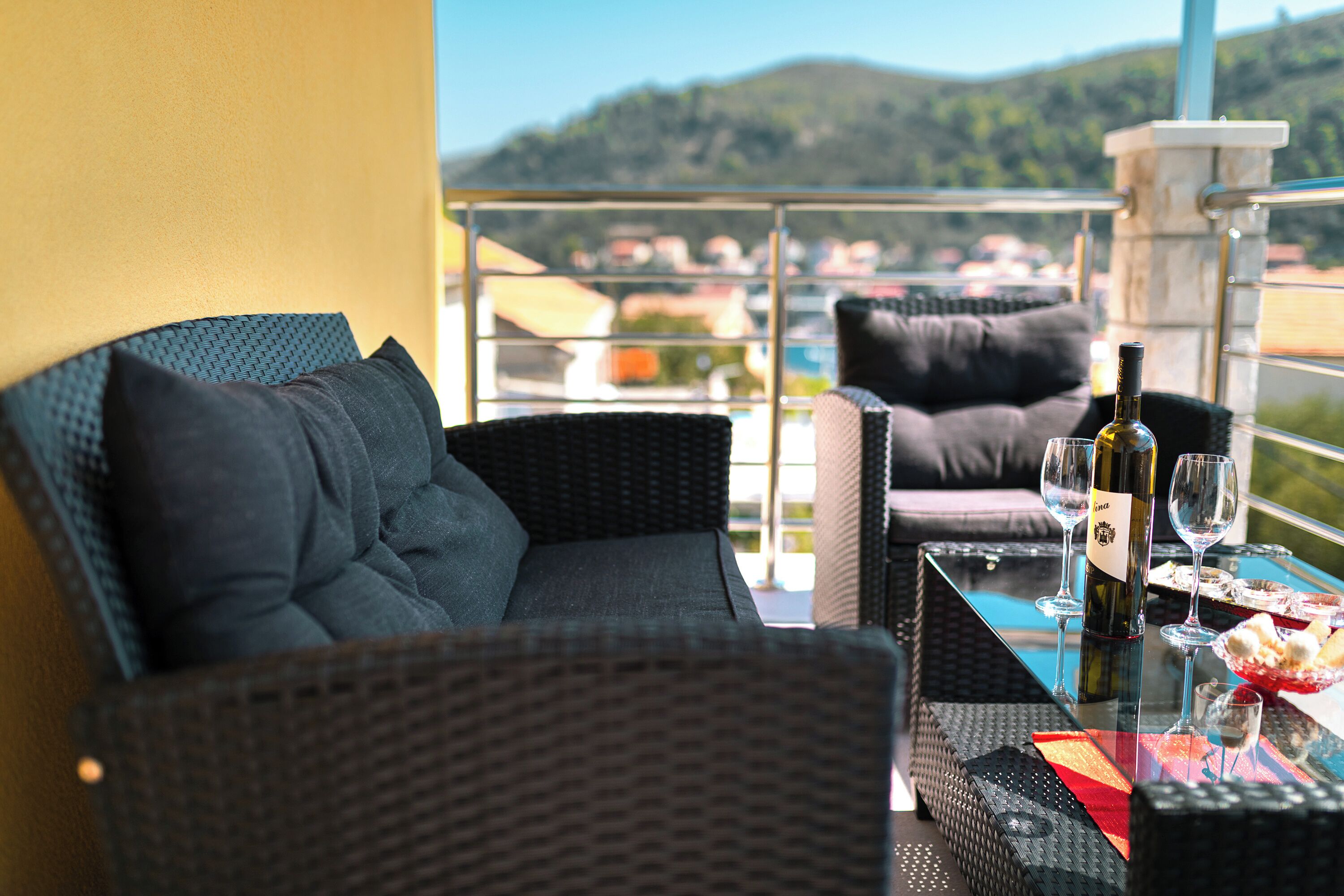 A balcony with wicker furniture, a glass table, and a bottle of wine.