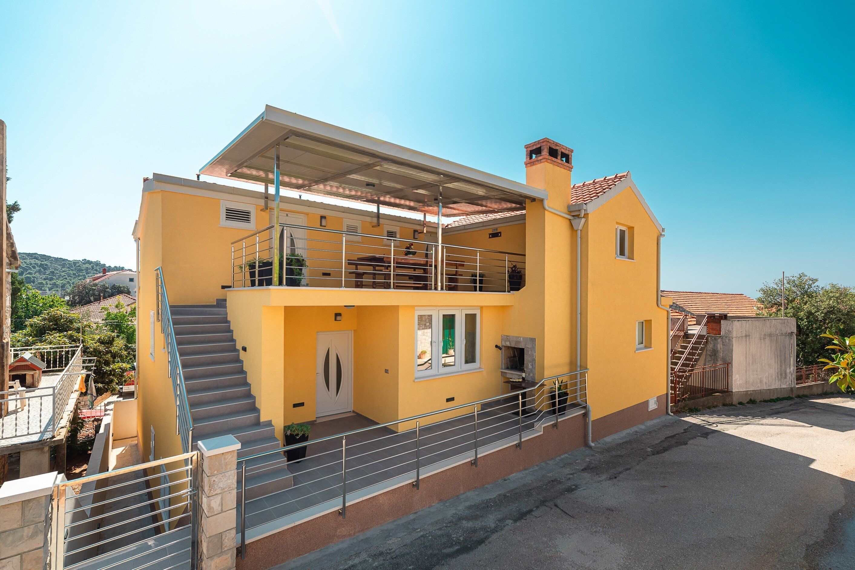 A two-story yellow building with a balcony, a staircase, and a chimney.