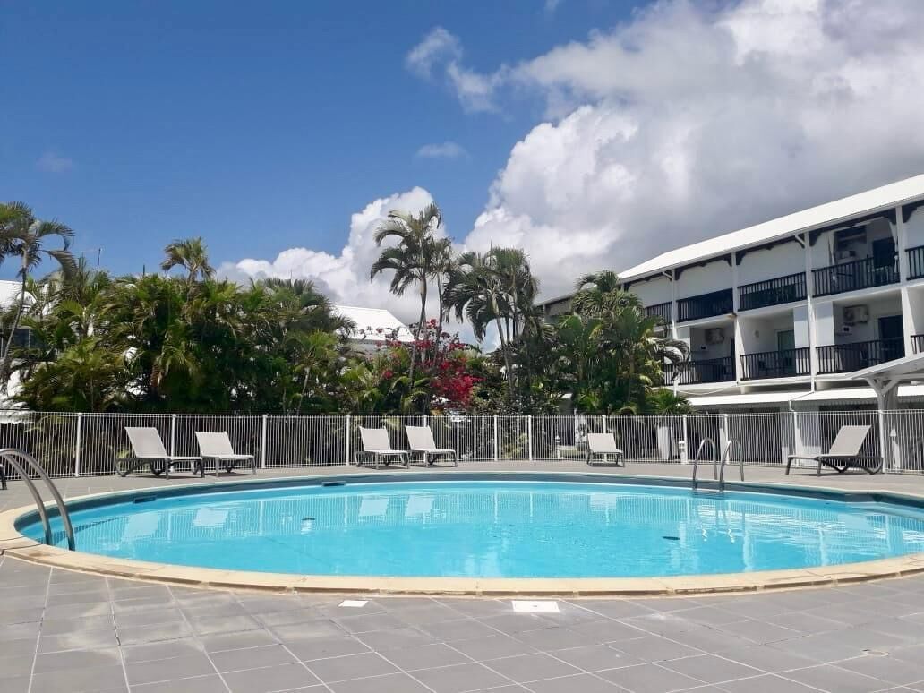 A swimming pool with lounge chairs, surrounded by palm trees and a multi-story building.