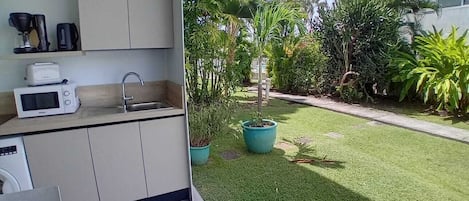 Une cuisine équipée d’un évier, d’un four à micro-ondes et d’une machine à café. Il y a une petite fenêtre et une plante en pot.