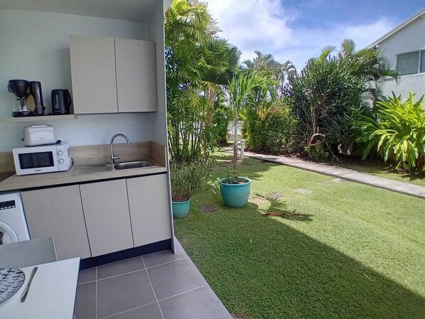 A kitchen with a sink, microwave, and coffee maker. There is a small window and a potted plant.