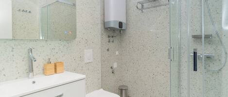 Ein Badezimmer mit Duschkabine aus Glas, einer weißen Toilette und einem Waschbecken mit Spiegel darüber.