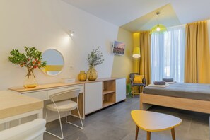 A modern hotel room with a bed, desk, chair, and a small table. There is a mirror, a vase with plants, and a picture on the wall. - Apartments Olea (Konavle)