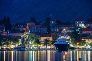 A waterfront scene with a large yacht docked near the shore, surrounded by buildings with red-tiled roofs and palm trees. - Apartments Olea (Konavle)