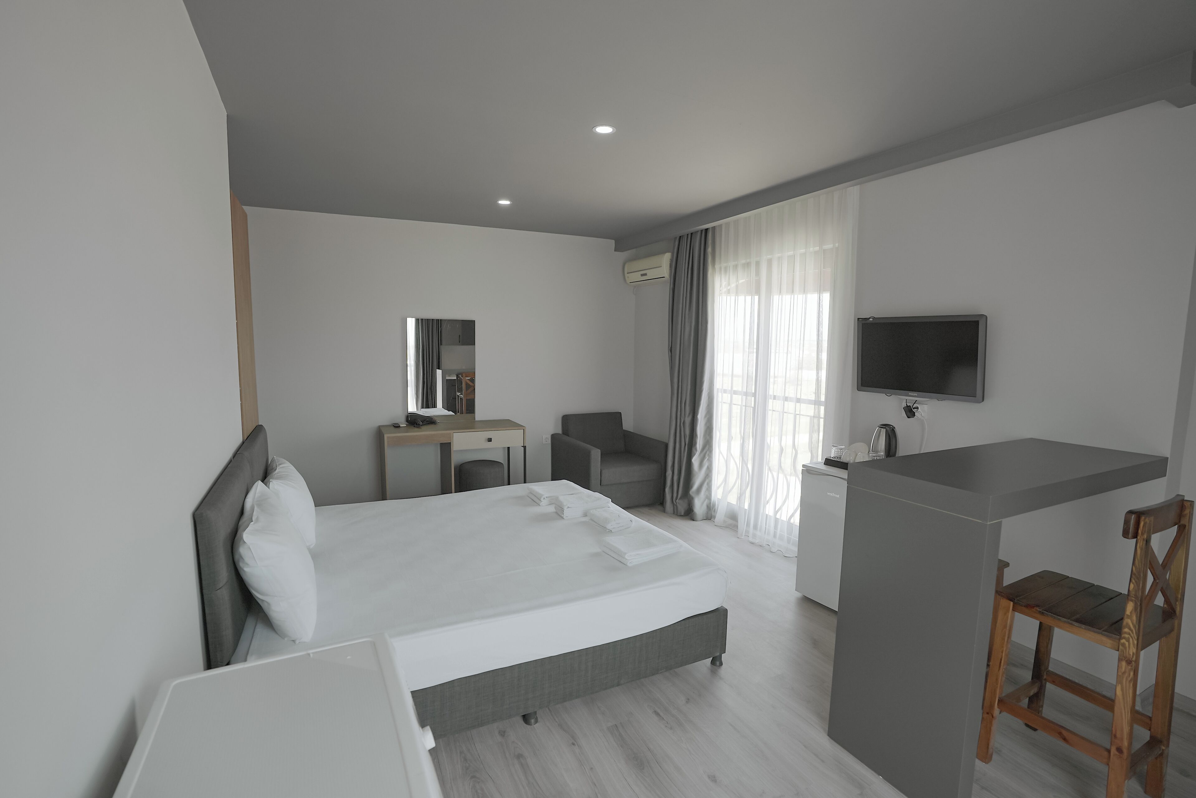 Una habitación de hotel moderna con una cama grande, un escritorio, una silla, un televisor y una kitchenette.