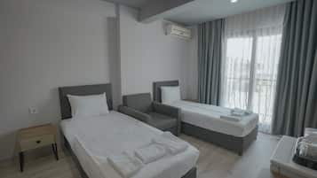 Hotelkamer met twee bedden, een nachtkastje, een stoel, een bureau met lamp en een raam met gordijnen.