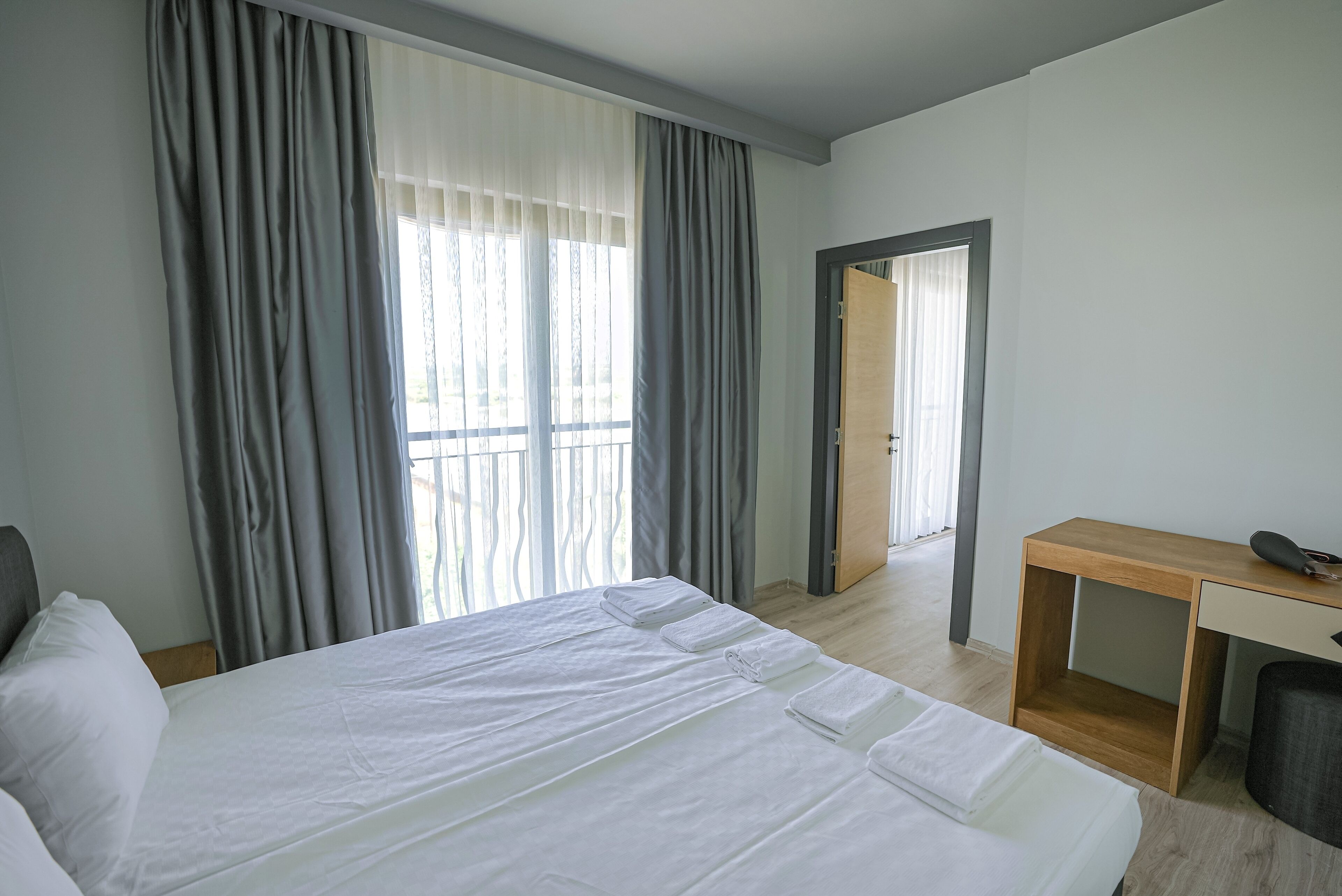 A hotel room with a large bed, a wooden desk, and a view of the outdoors through the window.