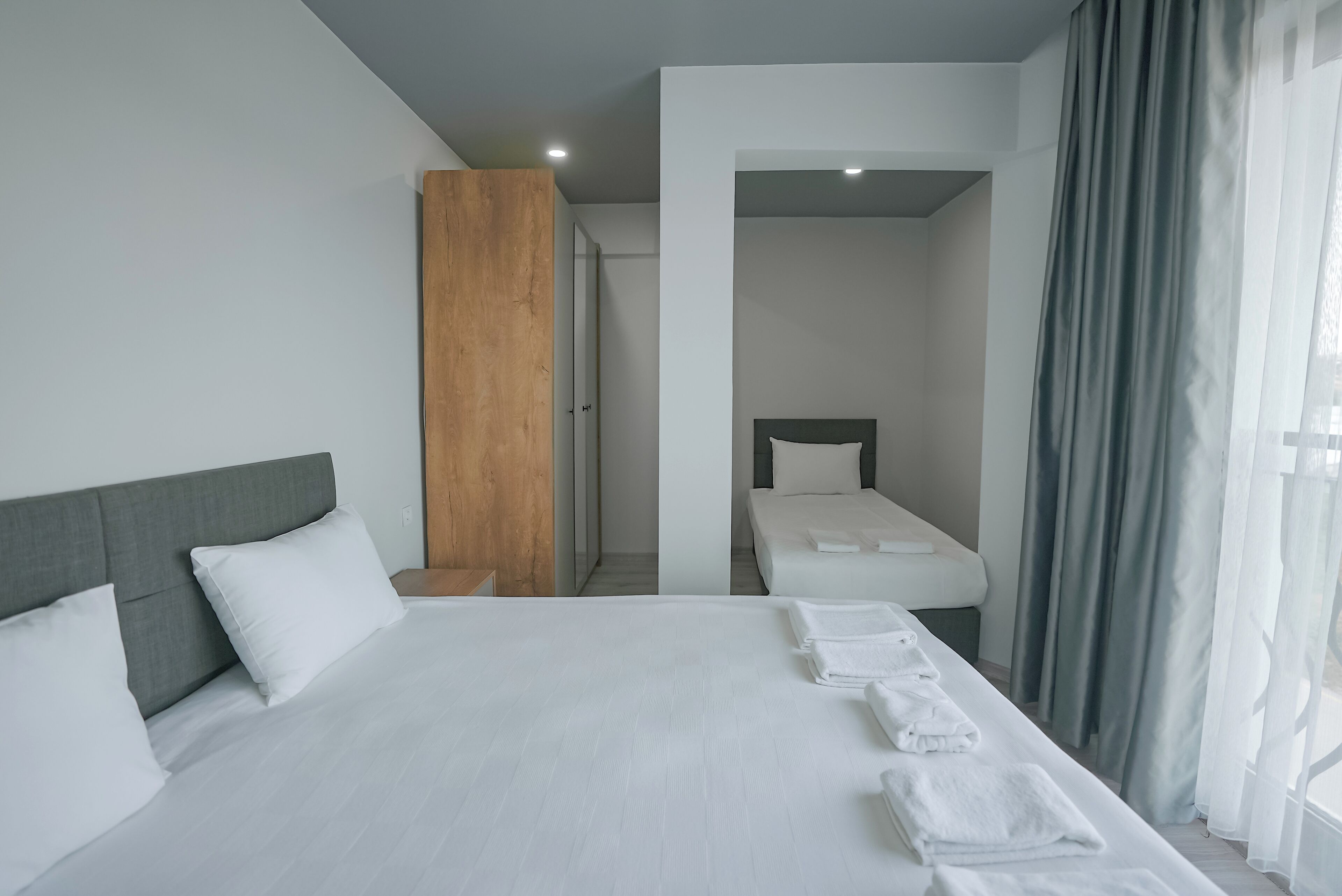 A modern hotel room with a large bed, a wooden accent wall, a separate sleeping area, and a view of the outdoors.