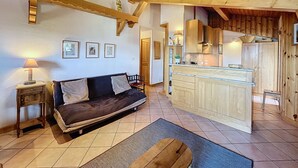 A cozy room with a wooden ceiling, a sofa, a small table, and a kitchen area with wooden cabinets and a countertop. - Modern Apartment with Mountain Views, Near Combloux Center (Combloux)