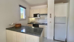 A kitchen with white cabinets, a microwave, a refrigerator, and a window with blinds.