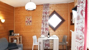 A cozy room with wooden walls, a dining table with chairs, a sofa, a coffee station, and a window with a view. - Studio for 2 in the heart of Les Orres 1650 with balcony and ski locker (Les Orres)