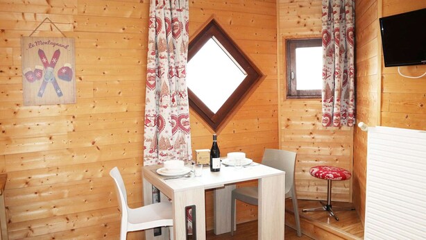 A cozy wooden cabin with a dining table set for two, a small stool, and a television mounted on the wall. - Studio for 2 in the heart of Les Orres 1650 with balcony and ski locker (Les Orres)