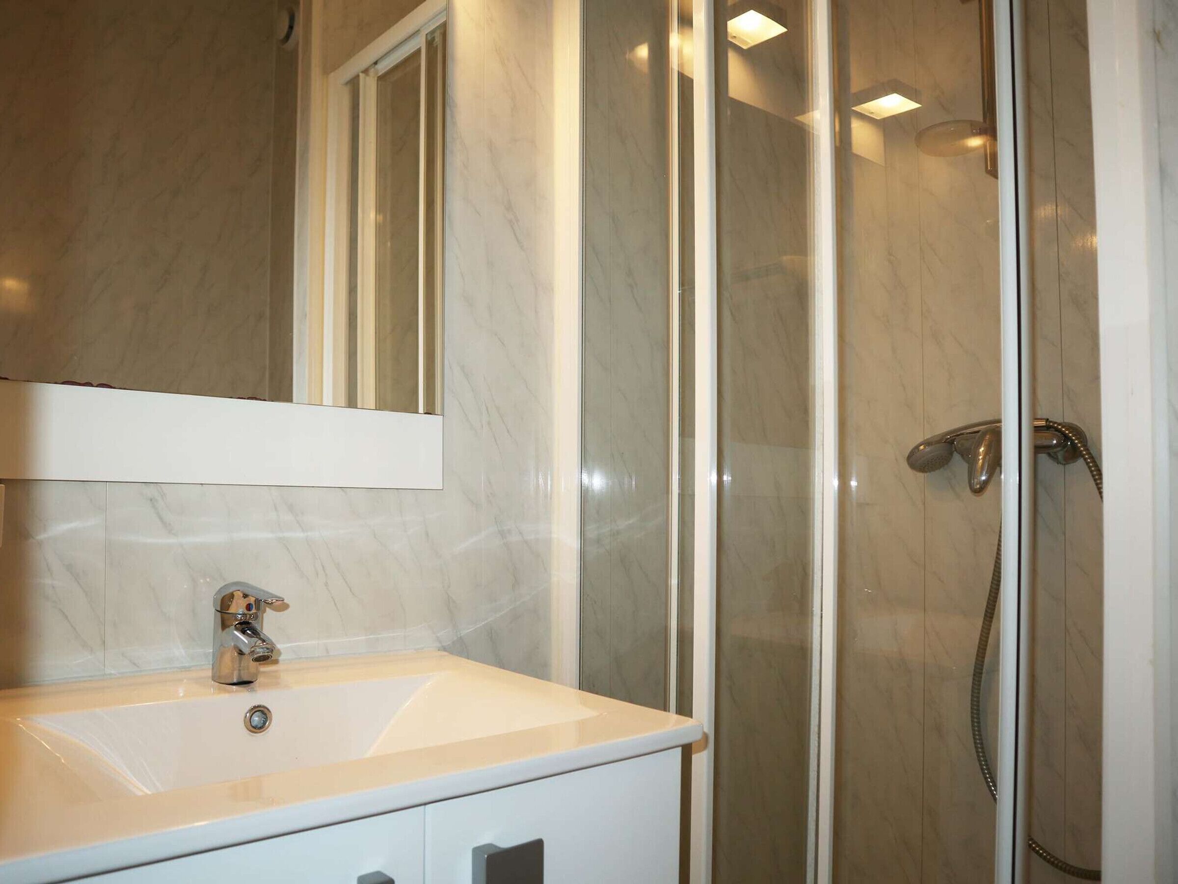Un baño con lavamanos de mármol, un espejo y una ducha con mampara de vidrio.