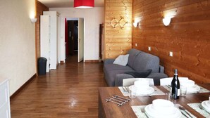 A wooden-floored living area with a dining table set for two, a sofa, and a red accent wall.